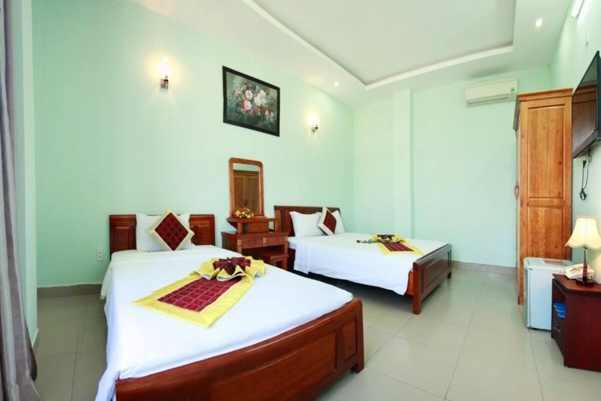 A hotel room with two wooden beds, a small desk, a mirror, and a window with curtains.