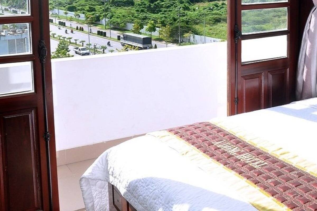 A bedroom with a bed, a window, and a view of a street and greenery.