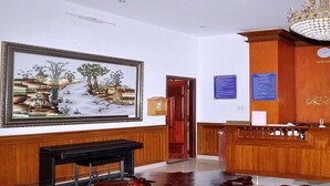 A reception area with a wooden reception desk, a chandelier, clocks displaying time in multiple cities, and a framed landscape painting. - A Dong Hotel (Da Nang)