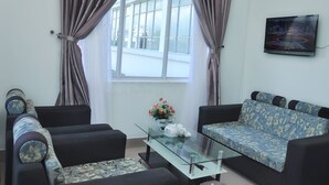 A living room with two sofas, a glass coffee table, a TV on the wall, and a window with curtains. - A Dong Hotel (Da Nang)
