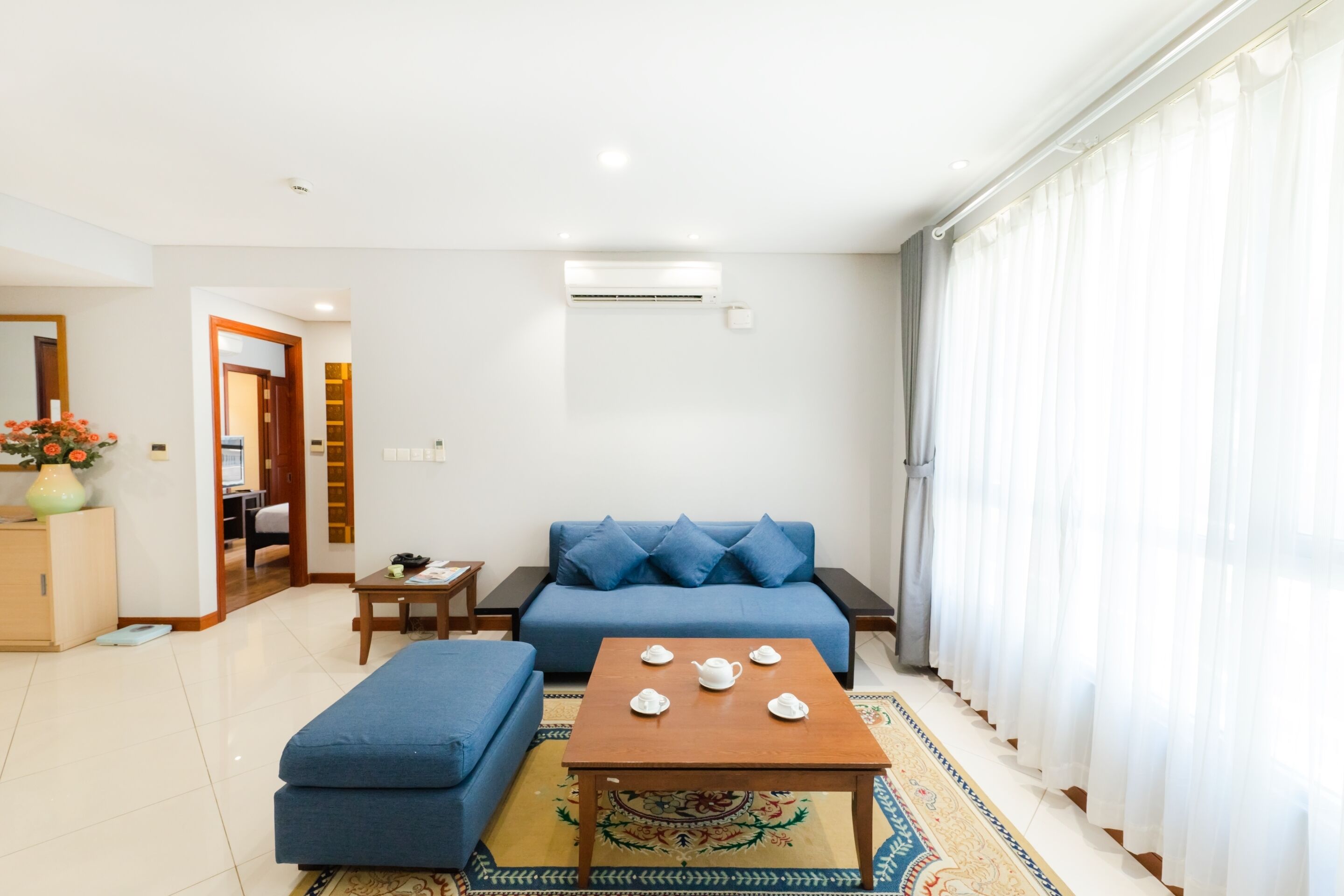 Una sala de estar moderna con un sofá azul, un reposapiés a juego, una mesa de centro de madera y una alfombra estampada.