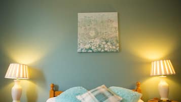 A bedroom with a bed, two bedside lamps, a floral artwork on the wall, and a blue fluffy pillow.