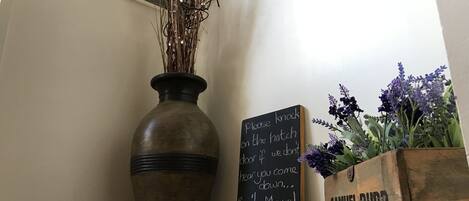 Un jarrón rústico con ramas secas, una pizarra con un mensaje y una maceta de madera con flores moradas.