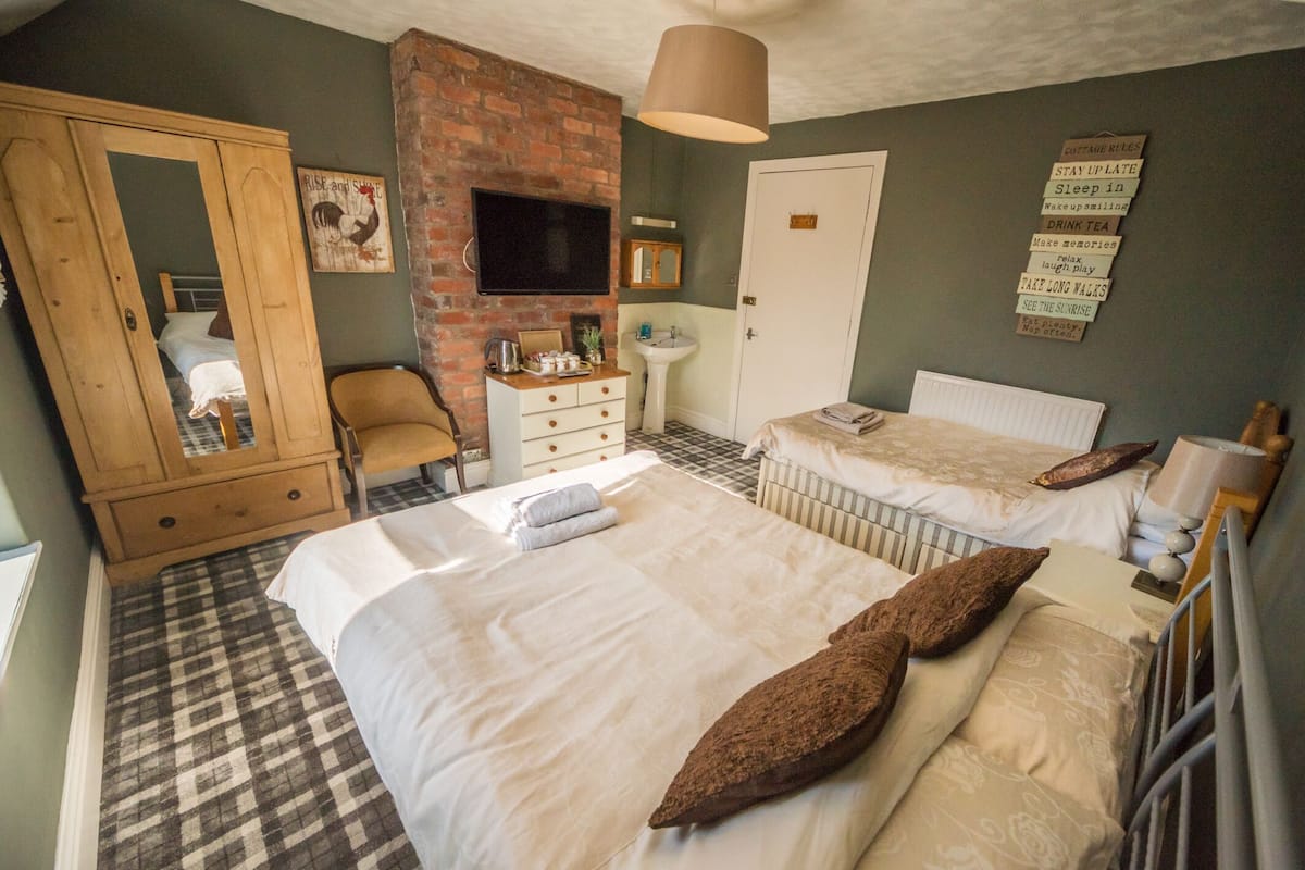 A bedroom with two beds, a wooden wardrobe, a desk, a chair, a television, and a wall-mounted sign with rules.