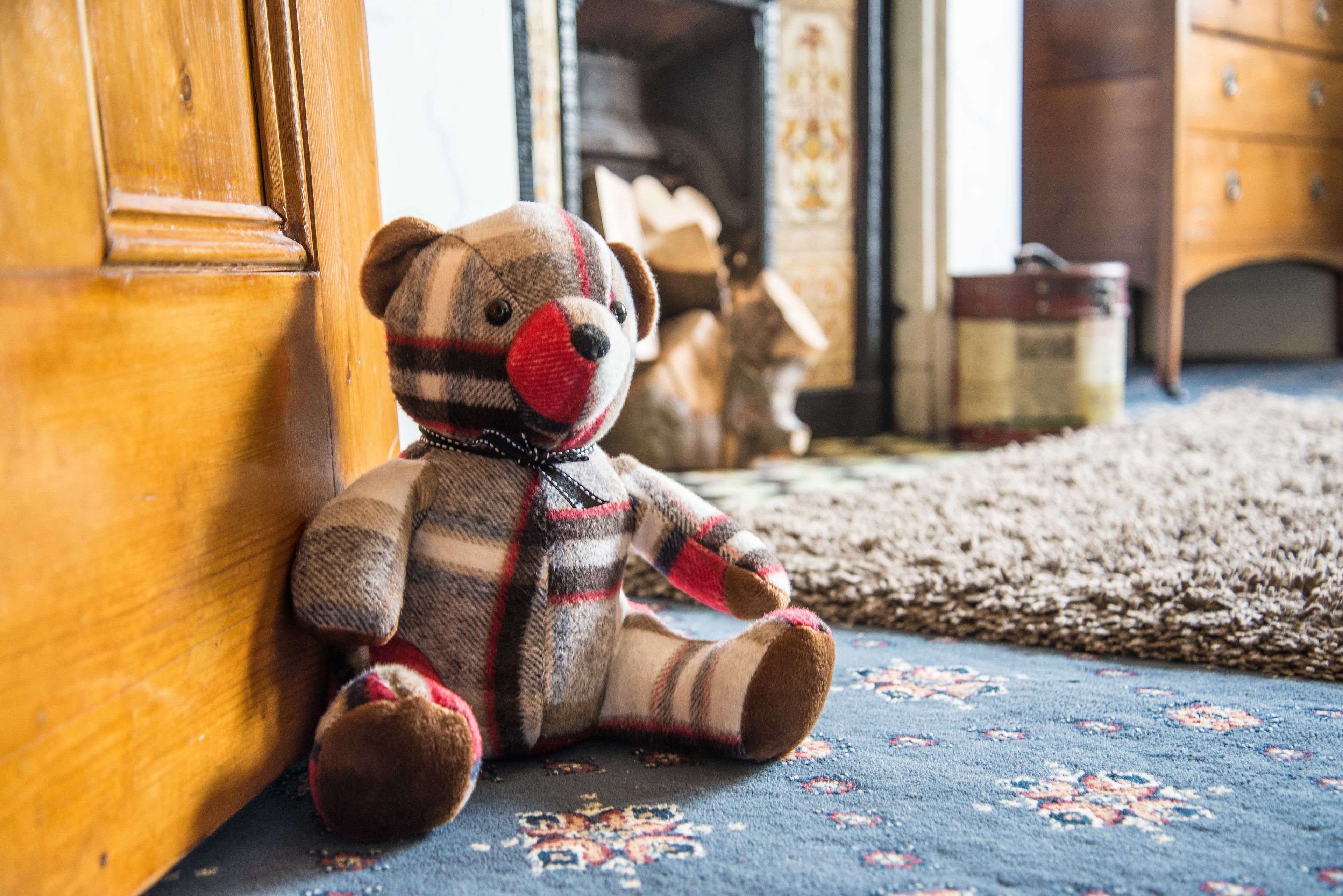 A plush toy bear sitting on a patterned carpet near a wooden door.