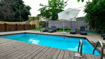 A wooden deck with a swimming pool, lounge chairs, and a covered umbrella.