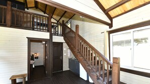 A wooden staircase leading to a second floor, a kitchen area with a refrigerator, and a bench near the entrance. - Tzlil Hateva (Ma'ale Yosef)