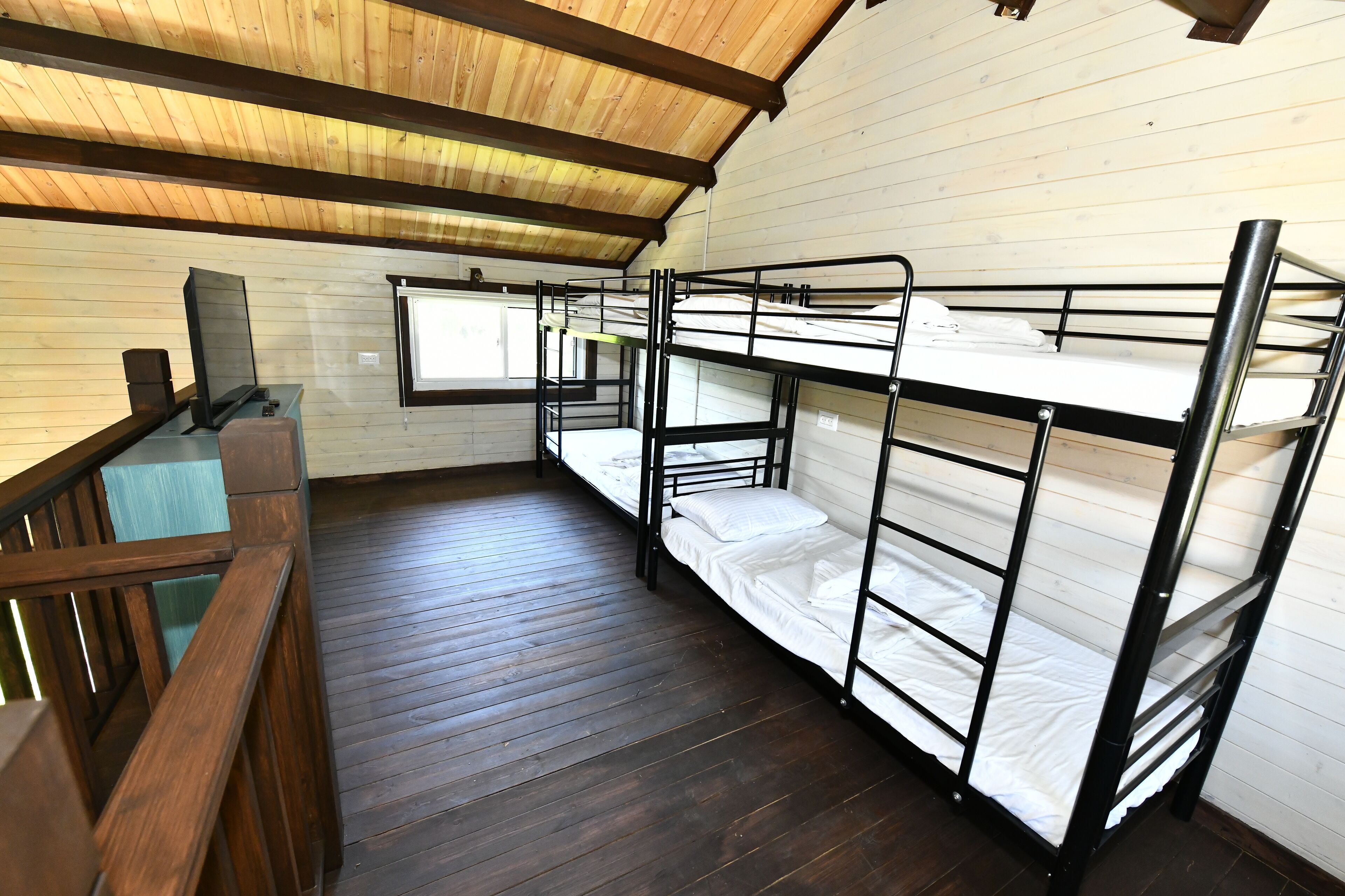 A dormitory room with bunk beds, wooden flooring, and a window.