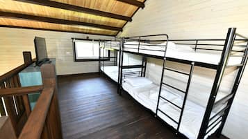 A dormitory room with bunk beds, wooden flooring, and a window.