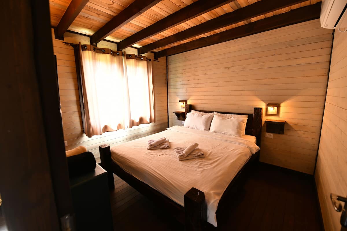 Camera da letto con rivestimento in legno, un letto, lampade sui comodini e una finestra con tende.