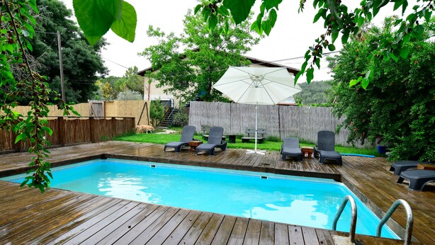 Una terraza de madera con piscina, sillas de descanso y un porche cubierto.