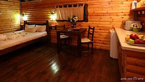 Acogedora habitación tipo cabaña de troncos con una cama, una mesa con sillas, una pequeña cocina y techo de madera.