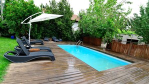 A wooden deck with a swimming pool, lounge chairs, and an umbrella. - Tzlil Hateva (Ma'ale Yosef)