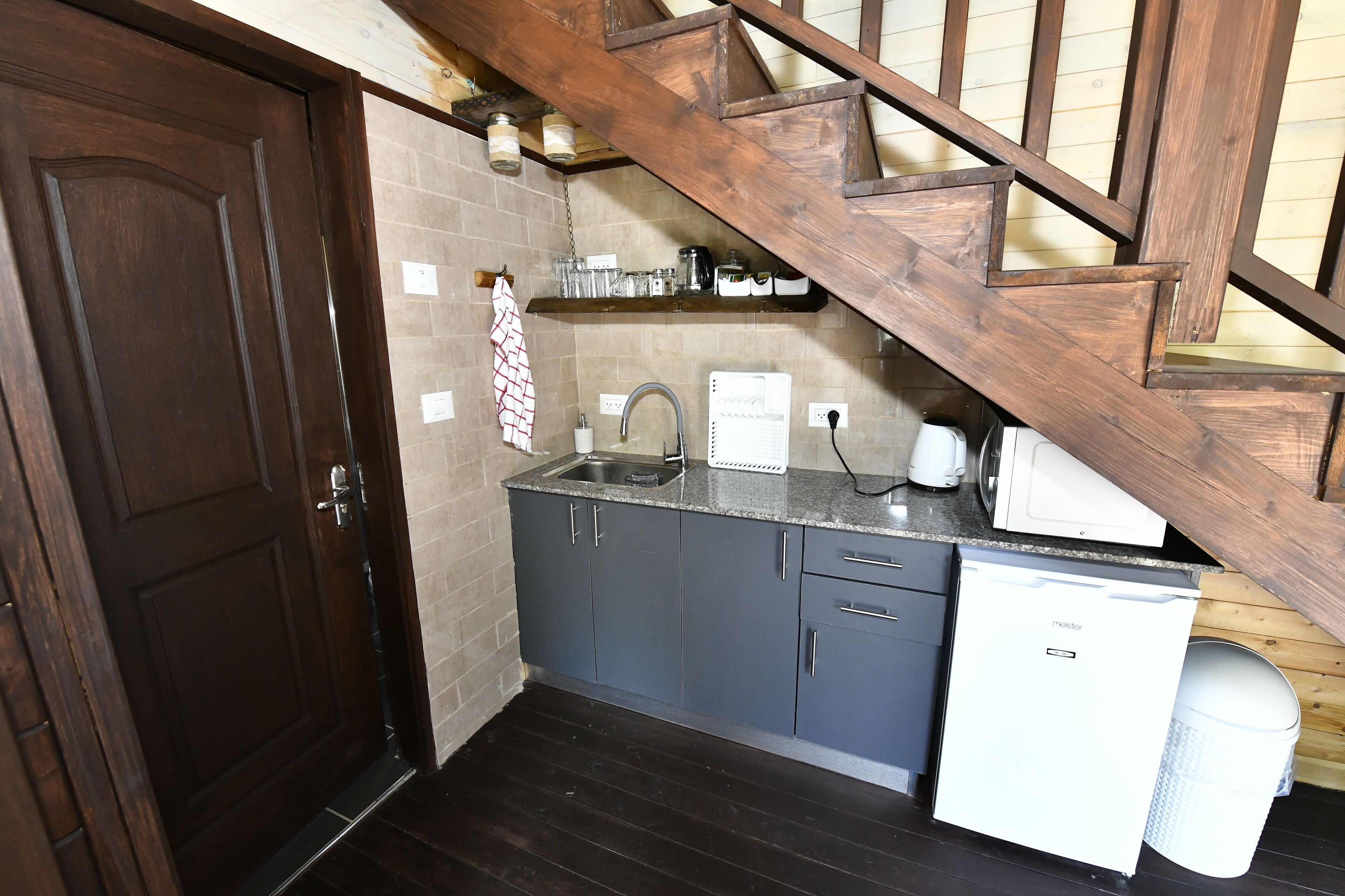 A compact kitchen with dark wooden cabinets, a built-in dishwasher, and a wooden staircase.