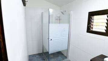 Un bagno con cabina doccia in vetro, pareti piastrellate di bianco e una panca in legno.