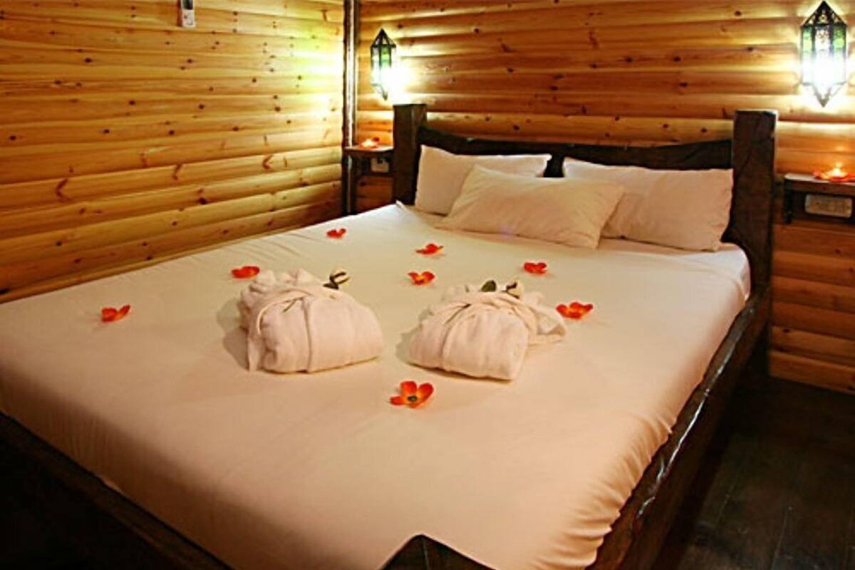 Una camera arredata in stile baita, con un letto, cuscini e un comodino con una lampada.