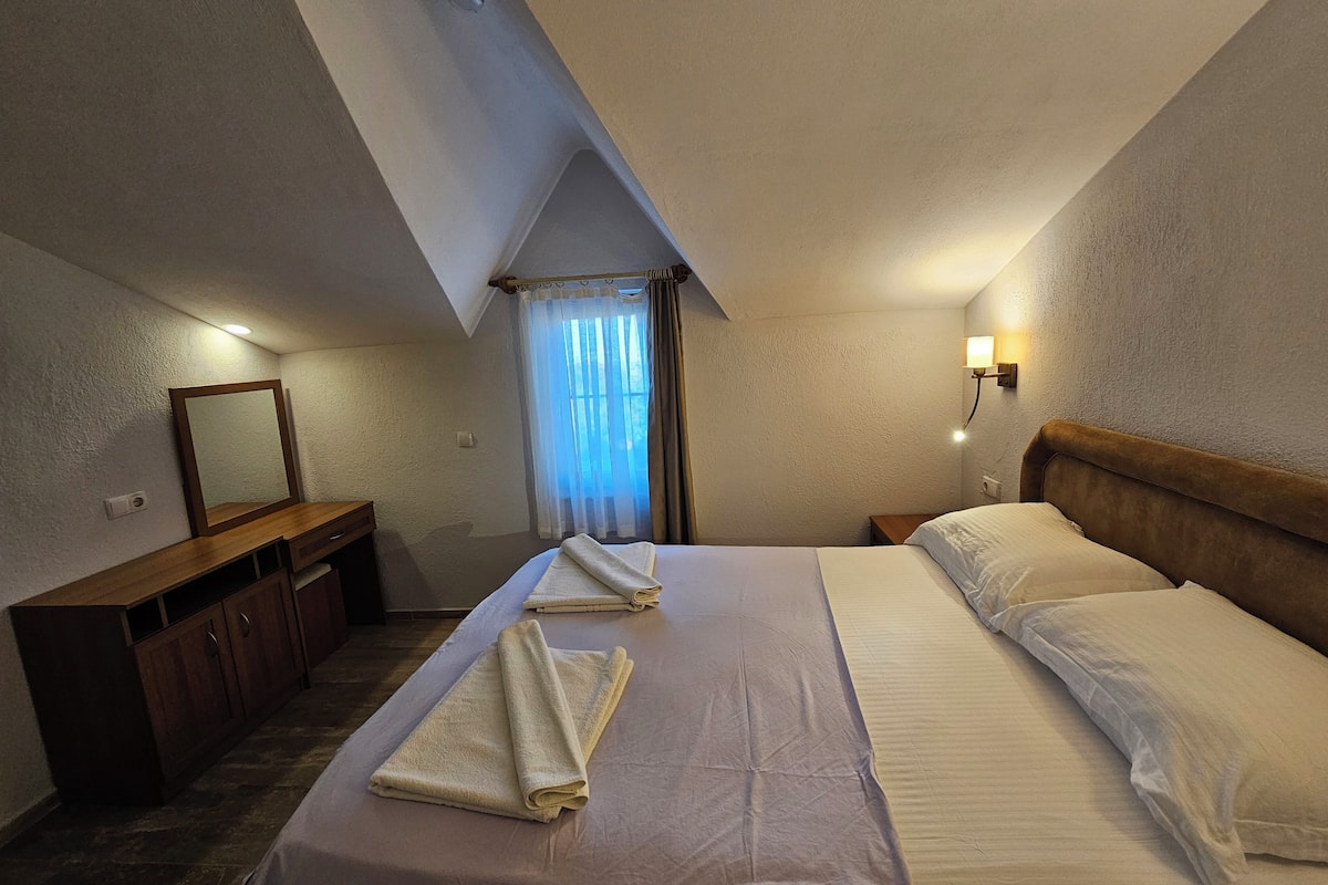 Une chambre d’hôtel avec un lit, un bureau, un miroir, une table de chevet et une fenêtre avec des rideaux.