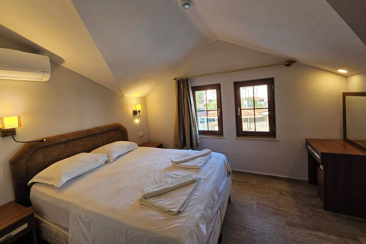 Une chambre d’hôtel avec un lit, une lampe de chevet, des fenêtres et un bureau.