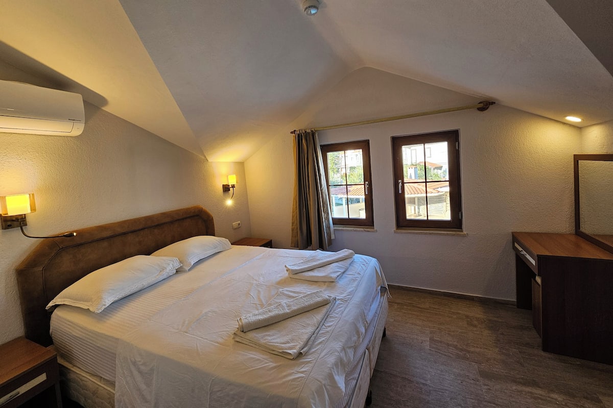 Une chambre d’hôtel avec un lit, une lampe de chevet, des fenêtres et un bureau.