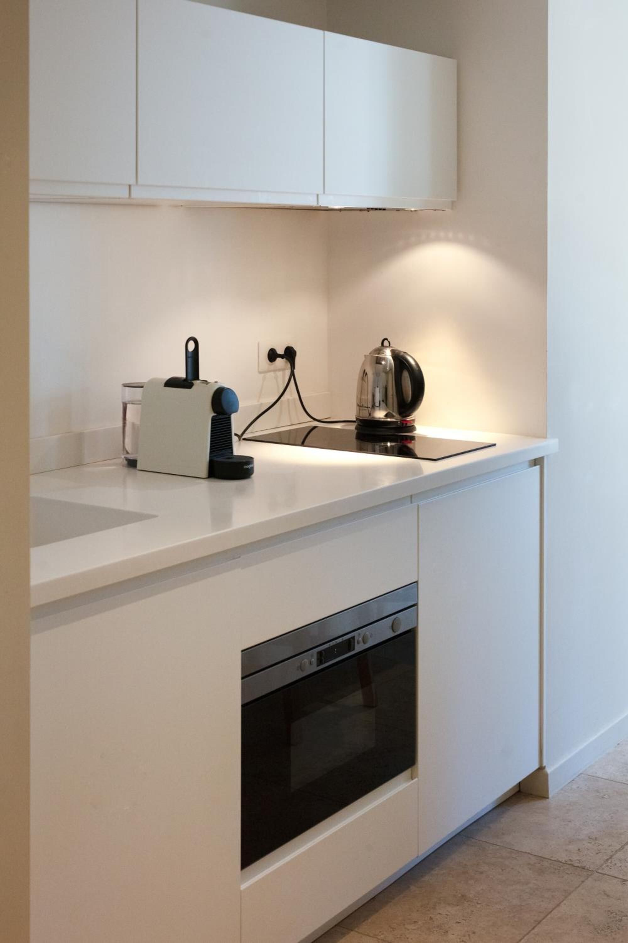 Een moderne keuken met witte kasten, een inbouwoven, een waterkoker en een broodrooster op het aanrecht.