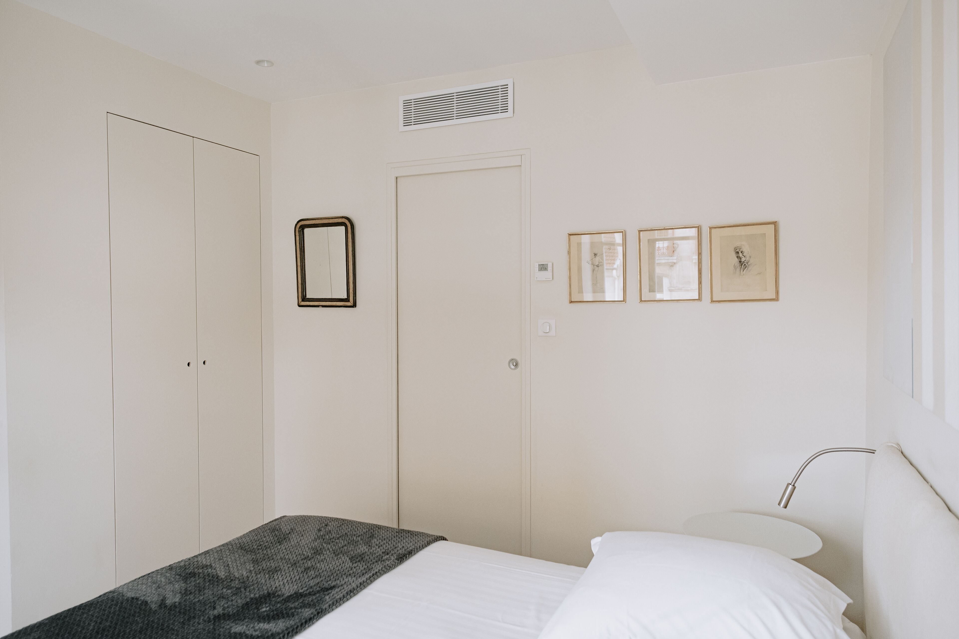 A bedroom with a bed, a bedside table, a lamp, a wardrobe, and three framed pictures on the wall.