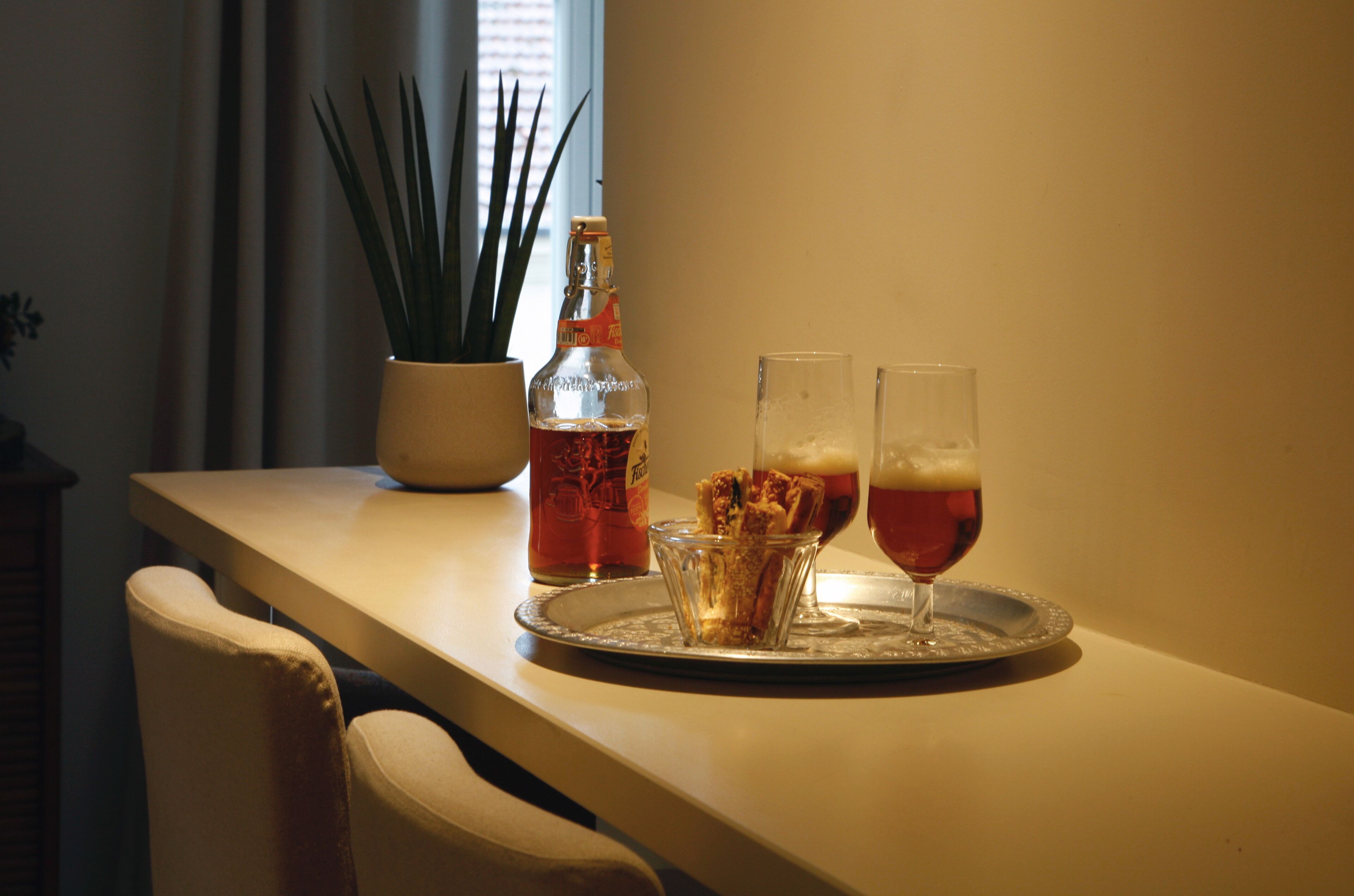 A tray with two glasses of beer and a bottle of liquor on a table.