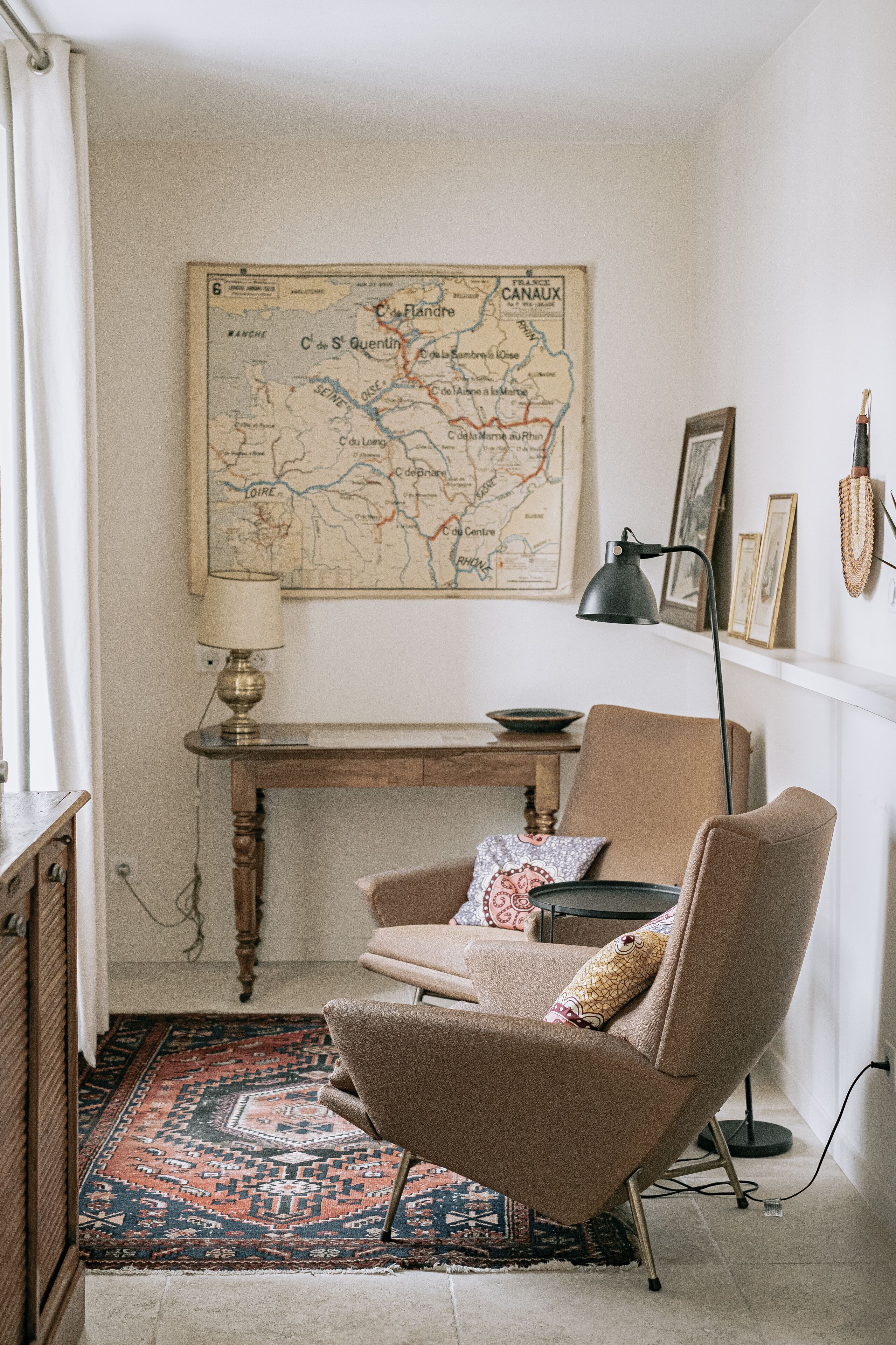 A room with a map on the wall, a desk, a chair, a lamp, and a patterned rug.