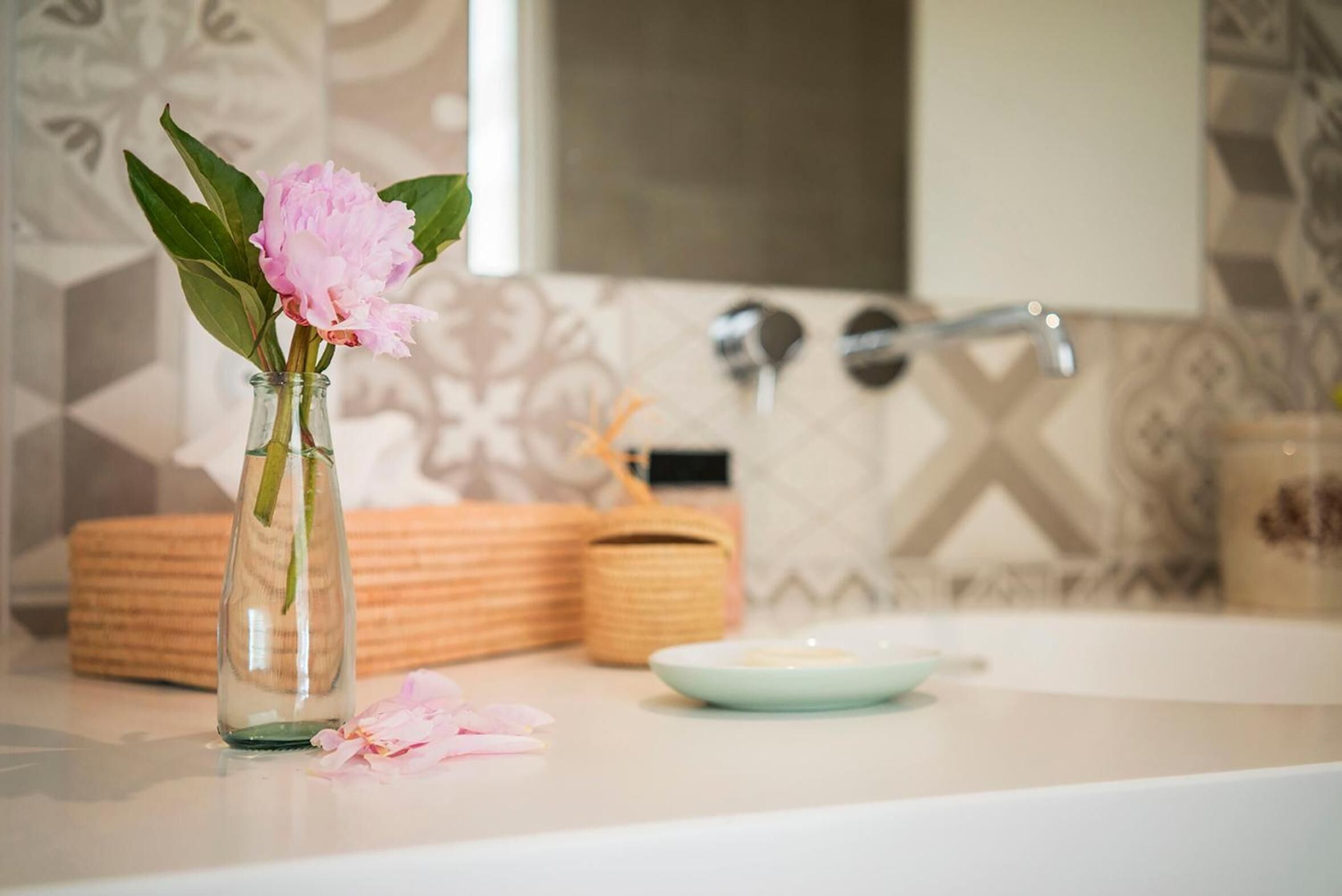 Un bagno con un vaso di vetro contenente fiori rosa, un portasapone e un cesto in vimini.