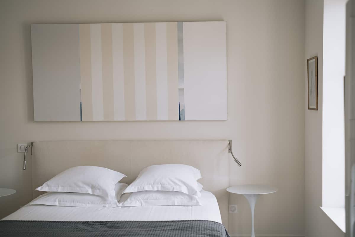 Minimalistiseen tyyliin sisustettu hotellihuone, jossa on suuri sänky, kaksi yöpöytää ja seinälle asennettu taideteos.