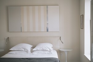 Habitación de hotel minimalista con una cama grande, dos mesitas de noche y una obra de arte colgada en la pared.