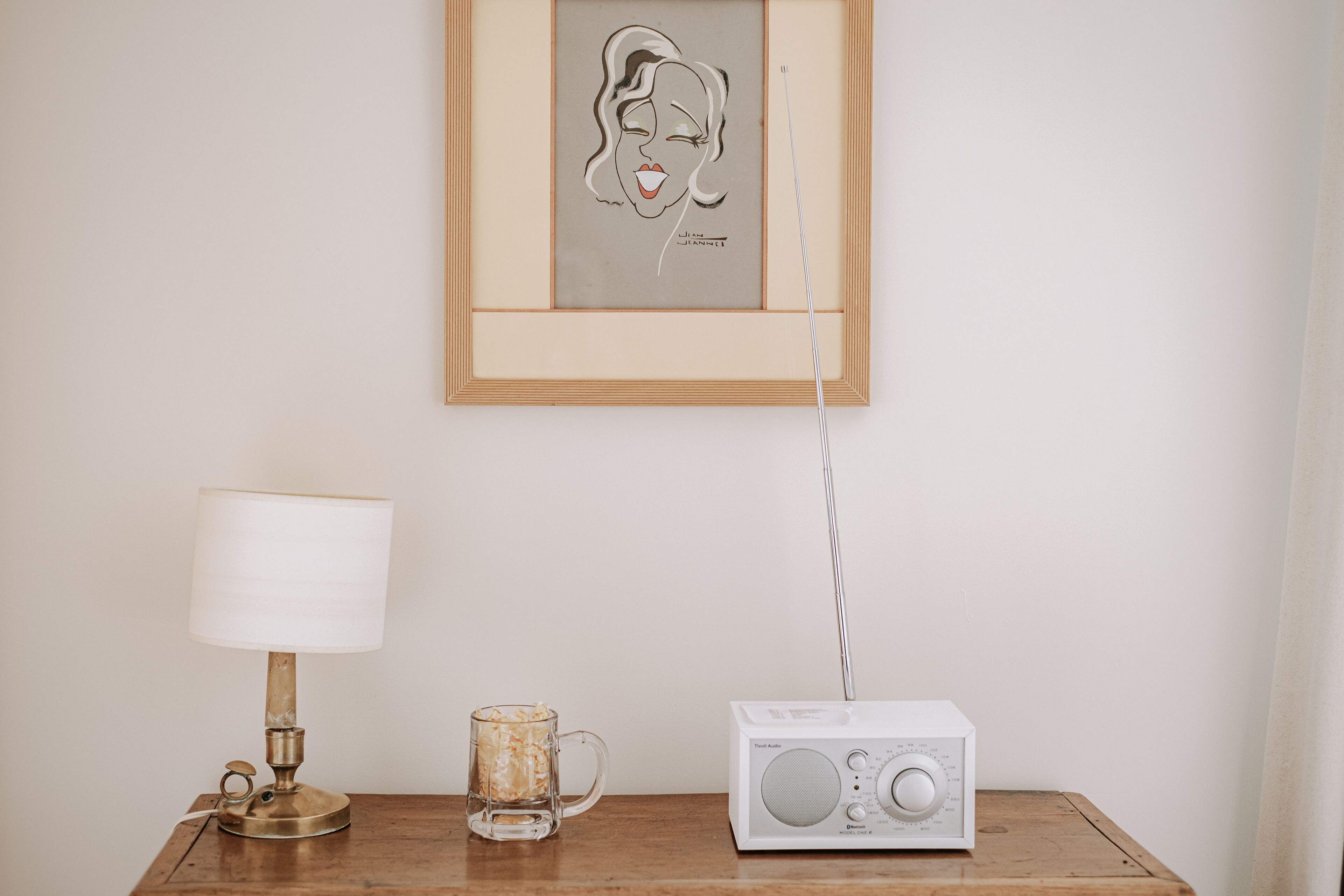 En inramad tavla på väggen, en bordslampa, en glasmugg och en gammal radio.