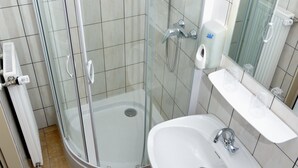 Een moderne badkamer met een douche met glazen wand, een witte wastafel en een spiegel.