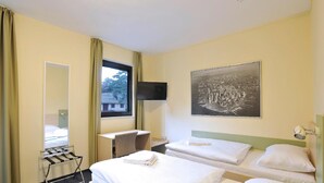Een hotelkamer met twee bedden, een bureau, een stoel, een televisie en een raam met gordijnen.