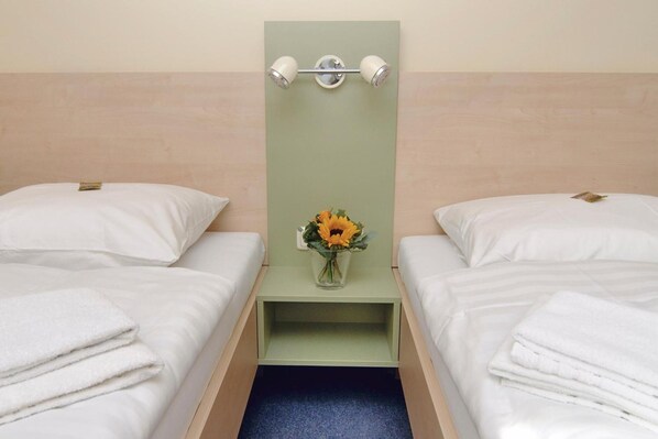 Habitación de hotel con dos camas individuales, una mesita con un florero y una lámpara de pared.