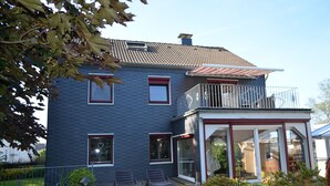 A two-story house with a balcony, a covered patio, and a glass door entrance. - Ferienwohnung Bergisch Land (Wermelskirchen)