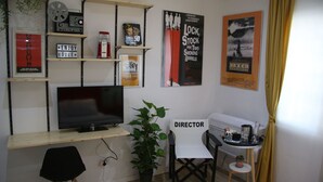 A small, well-organized room with a TV, a director's chair, a desk, and various movie posters on the wall. - Mila Guest House (Rome)