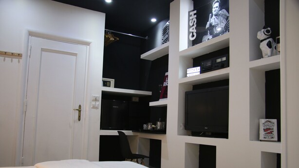 A bedroom with a bed, a desk with a computer, and shelves with various items. - Mila Guest House (Rome)