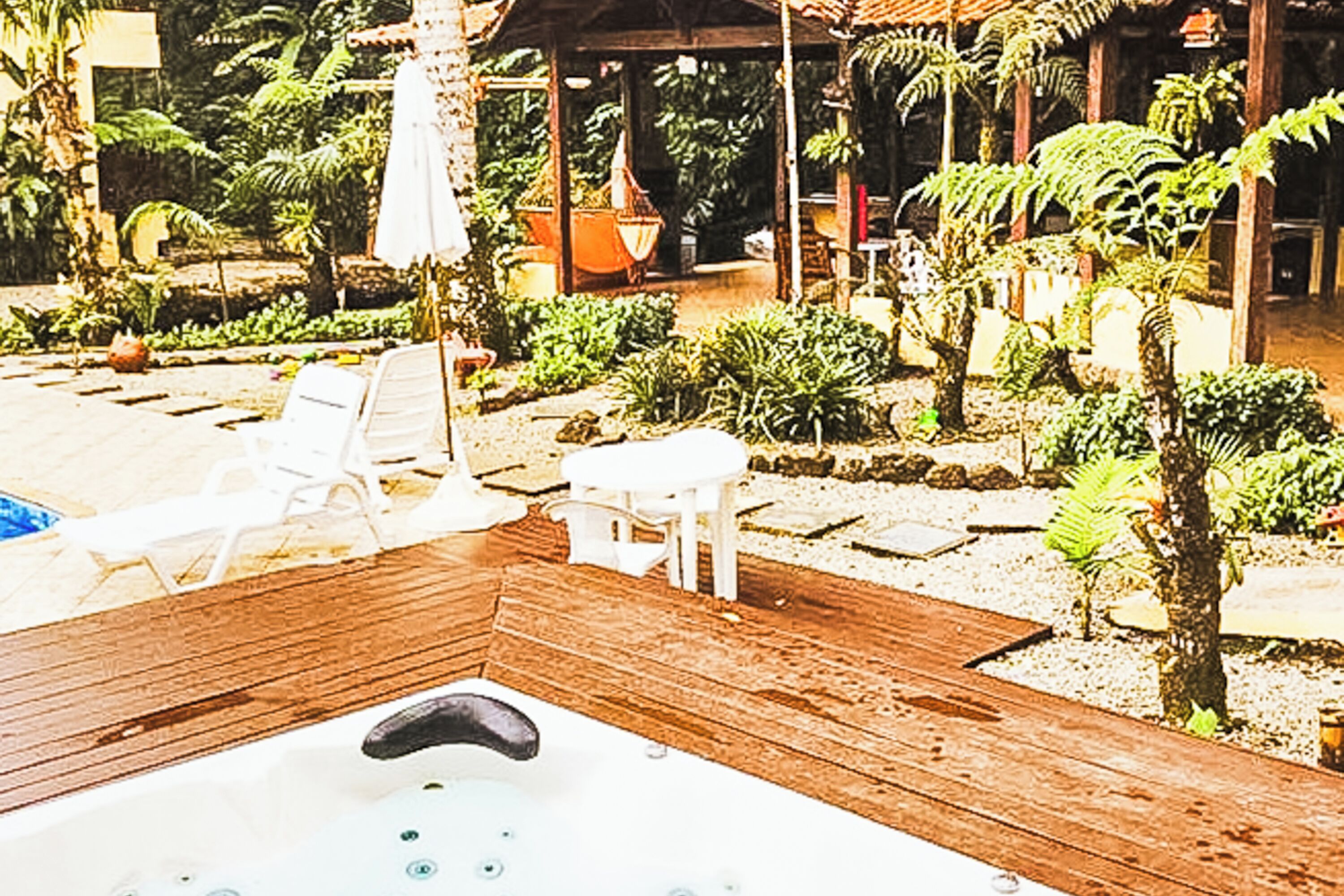 Terraza de madera con jacuzzi, rodeada de sillones de descanso y un jardín con diversas plantas.