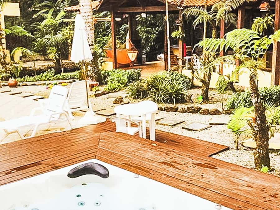 A wooden deck with a hot tub, surrounded by lounge chairs and a garden with various plants.