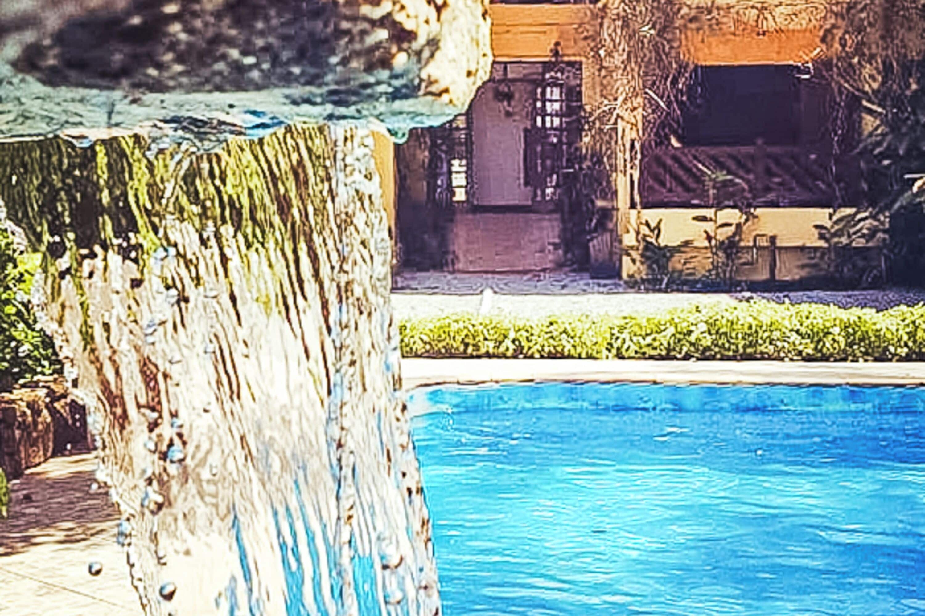 Una piscina con cascada y un edificio al fondo.