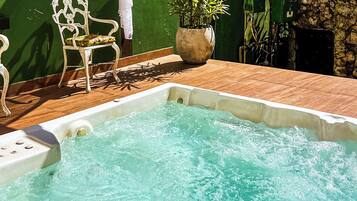 Uma banheira de hidromassagem com um deck de madeira, uma cadeira branca e um vaso com planta.
