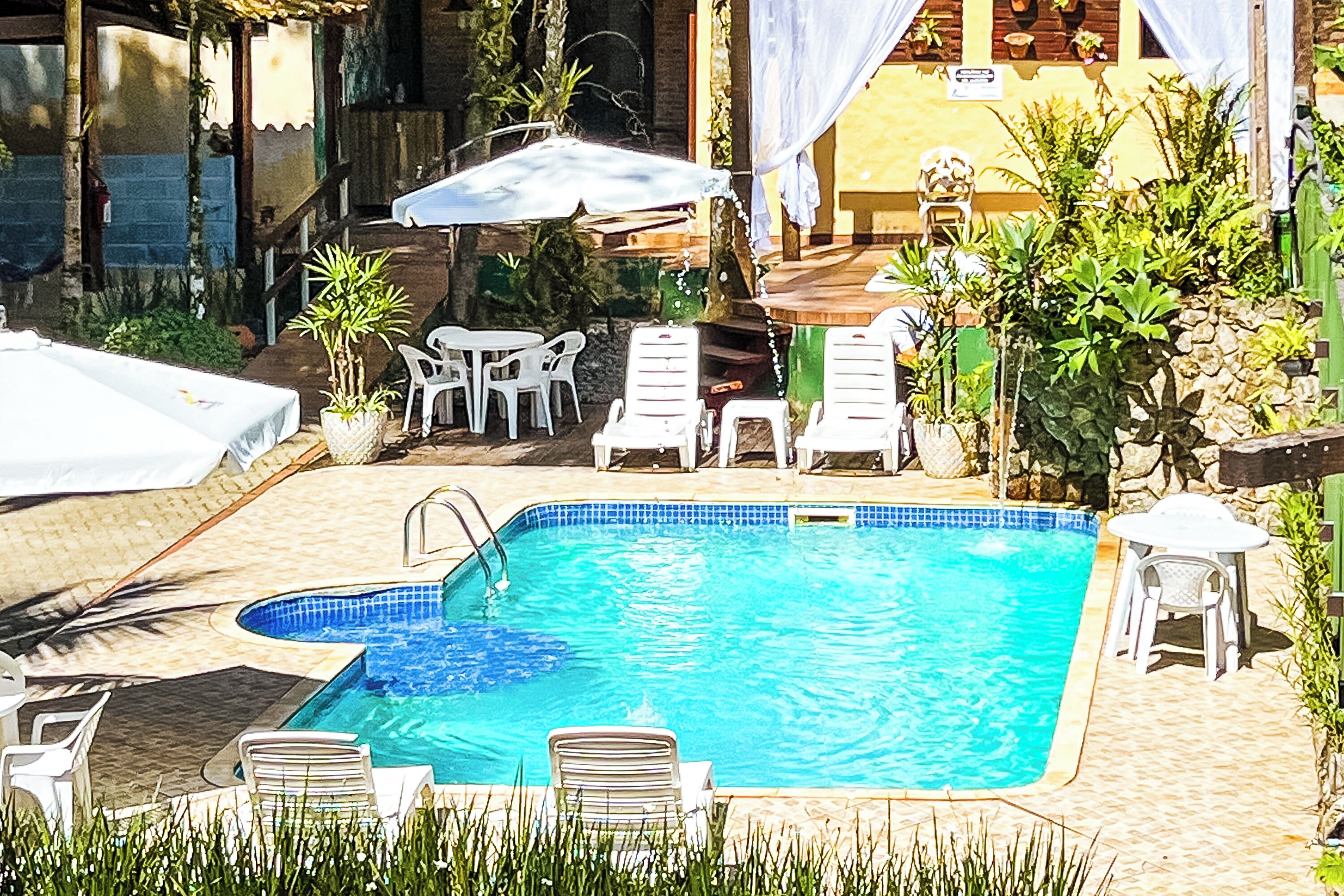 Ein Swimmingpool mit Liegestühlen und einem Tisch, umgeben von Kübelpflanzen und einer überdachten Sitzgruppe.