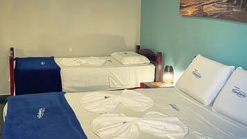 Quarto de hotel com duas camas de solteiro, cada uma com lençóis e almofadas brancas, um cobertor azul em uma cama e uma mesa de cabeceira com abajur.