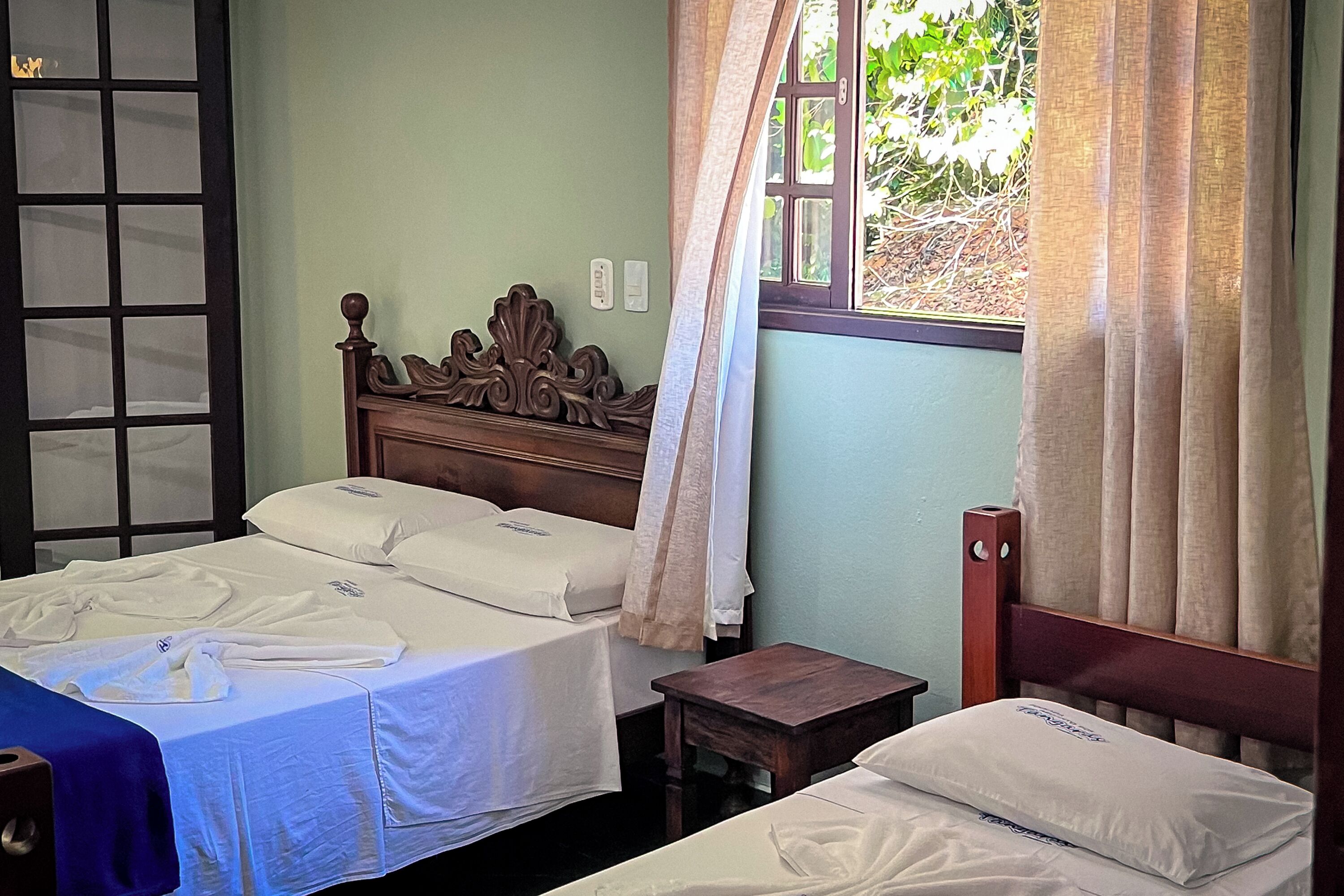 A room with two beds, a wooden headboard, a small table, and a window with curtains.