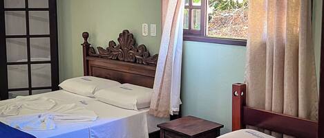 A room with two beds, a wooden headboard, a small table, and a window with curtains.