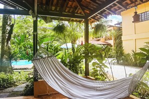 Un hamac suspendu sous une structure en bois, avec vue sur une piscine et une végétation luxuriante.
