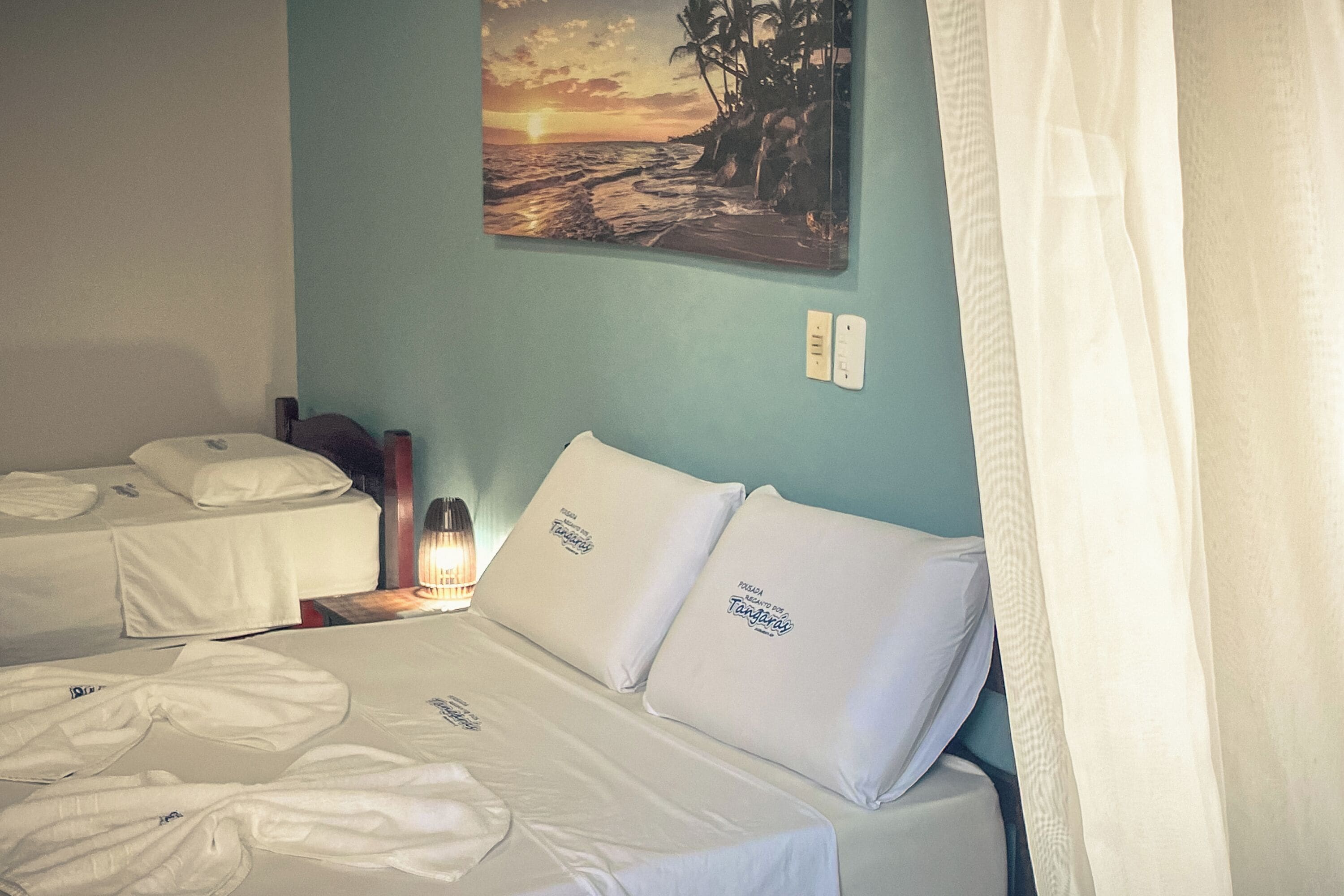 Habitación de hotel con dos camas, un cuadro de un atardecer y una mesita de noche con lámpara.