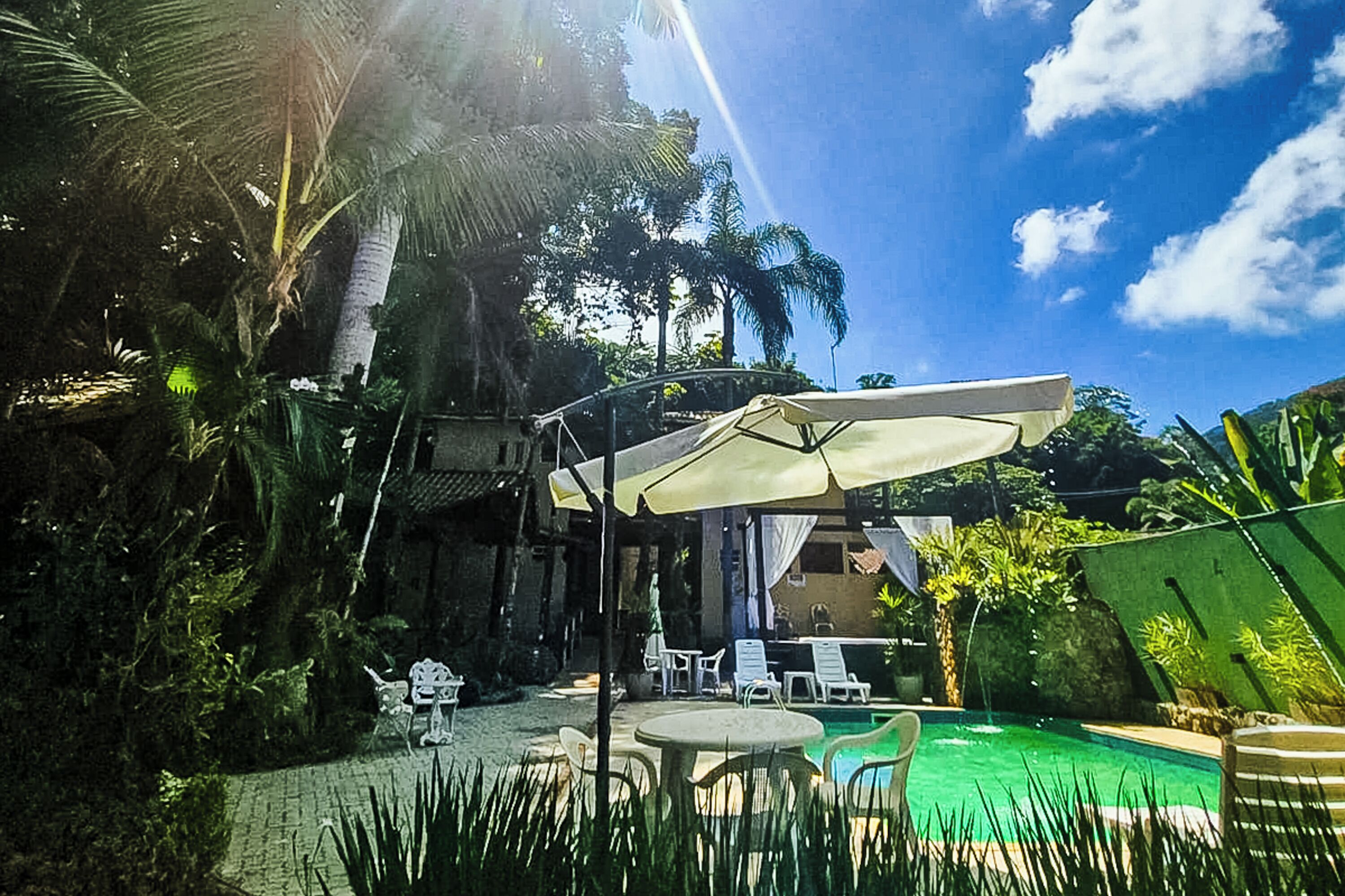 A pool area with a covered seating area, lounge chairs, and a clear sky.