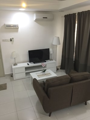 A modern living room with a flat-screen TV, white entertainment unit, brown sofa, and a coffee table with a potted orchid. - Akasia Apartment (Pelabuhan Klang)