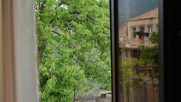 A view through a window with a wooden fence and a house with a balcony. - Hotel Bagineti (Mtskheta)